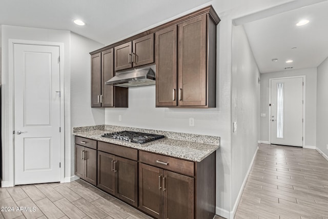 kitchen featuring dark brown cabinets, light stone counters, stainless steel gas stovetop, and light hardwood / wood-style flooring