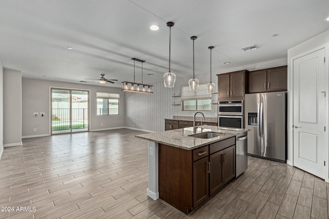 kitchen featuring decorative light fixtures, ceiling fan, appliances with stainless steel finishes, sink, and light stone counters