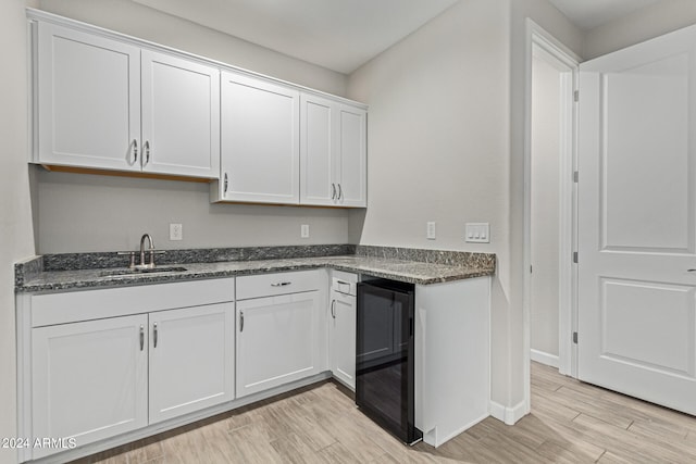 kitchen featuring dark stone counters, light hardwood / wood-style floors, wine cooler, sink, and white cabinets