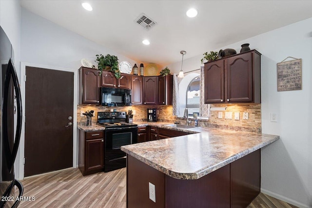 kitchen featuring black appliances, sink, kitchen peninsula, hanging light fixtures, and light hardwood / wood-style flooring