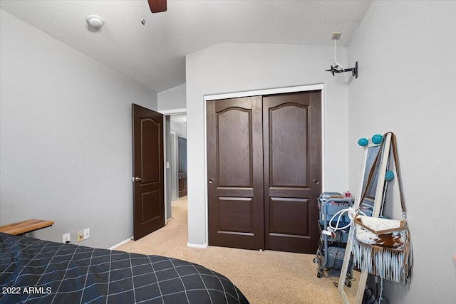 bedroom featuring a closet, light carpet, vaulted ceiling, a textured ceiling, and ceiling fan