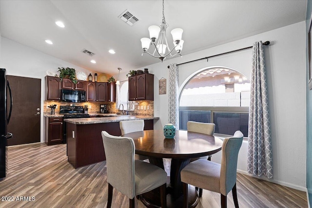 dining room with sink, light hardwood / wood-style flooring, vaulted ceiling, and a chandelier