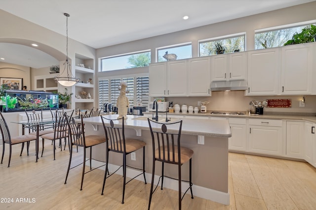 kitchen featuring decorative light fixtures, light hardwood / wood-style flooring, a center island with sink, white cabinets, and stainless steel gas stovetop