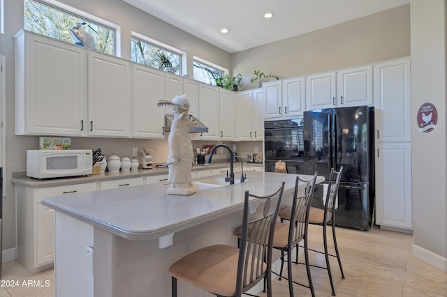 kitchen featuring an island with sink, sink, white cabinets, and black appliances