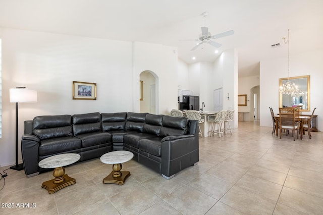 living room featuring arched walkways, light tile patterned floors, ceiling fan with notable chandelier, and a towering ceiling