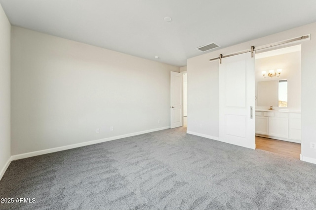 unfurnished bedroom with baseboards, a barn door, visible vents, and carpet flooring