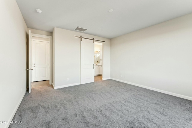 unfurnished bedroom featuring a barn door, baseboards, visible vents, ensuite bath, and carpet flooring