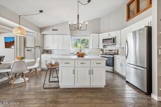 kitchen featuring white cabinetry, stainless steel appliances, decorative light fixtures, and dark wood-type flooring