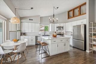 kitchen with white cabinetry, appliances with stainless steel finishes, decorative light fixtures, and a center island