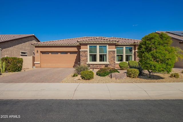 view of front facade featuring a tiled roof, stucco siding, decorative driveway, stone siding, and an attached garage