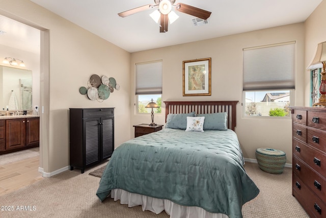 bedroom with visible vents, baseboards, light colored carpet, and ensuite bath