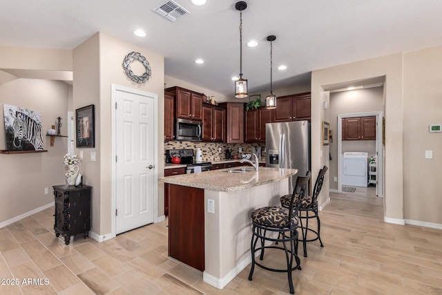 kitchen featuring visible vents, washer / clothes dryer, tasteful backsplash, a kitchen breakfast bar, and appliances with stainless steel finishes