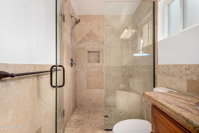 bathroom with vanity, toilet, tile walls, and a shower with shower door