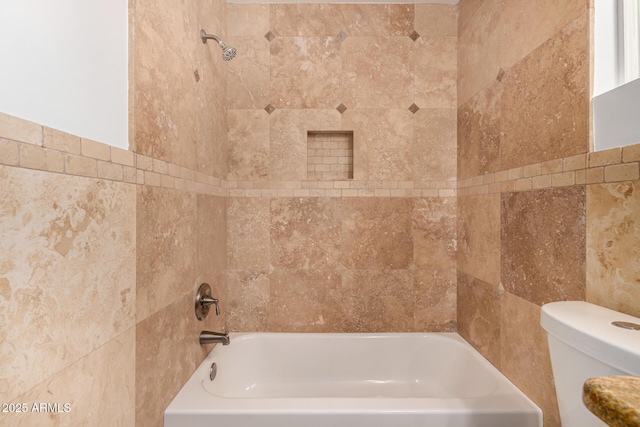 bathroom featuring toilet, tiled shower / bath, and tile walls