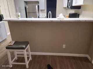 kitchen with dark wood-type flooring, white cabinets, fridge, and a kitchen breakfast bar