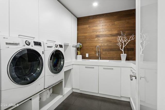 clothes washing area featuring separate washer and dryer, dark tile patterned floors, cabinets, wooden walls, and sink