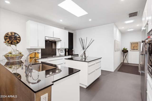 kitchen featuring sink, backsplash, white cabinets, a skylight, and a kitchen island