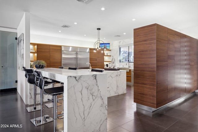 kitchen with a kitchen breakfast bar, hanging light fixtures, a large island, light stone countertops, and built in fridge