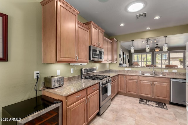 kitchen with visible vents, light stone countertops, decorative light fixtures, appliances with stainless steel finishes, and a sink