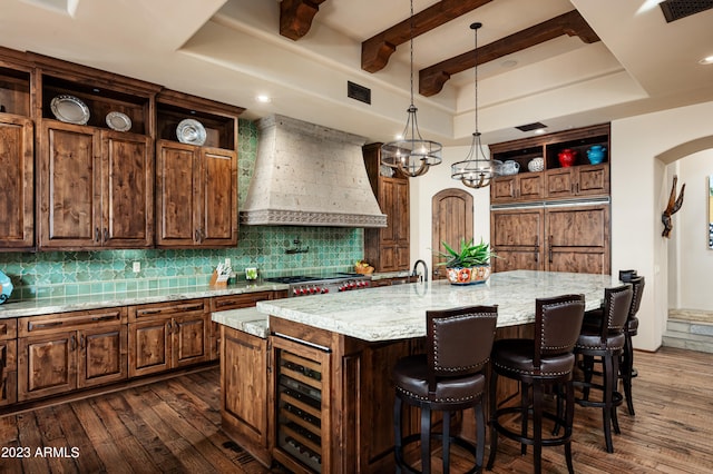 kitchen with backsplash, an island with sink, hanging light fixtures, and custom exhaust hood