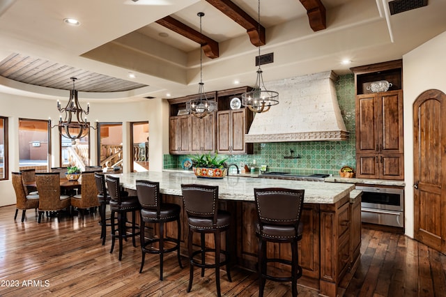 kitchen featuring custom range hood, dark wood-type flooring, a center island with sink, and light stone countertops