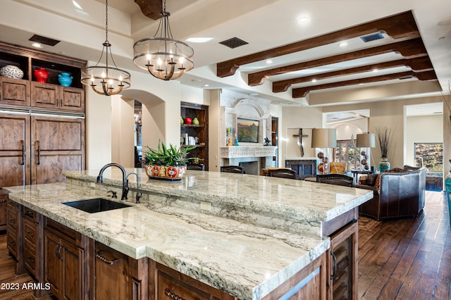 kitchen with beamed ceiling, sink, a center island with sink, light stone counters, and pendant lighting