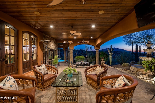 patio terrace at dusk featuring a mountain view, an outdoor hangout area, ceiling fan, and french doors