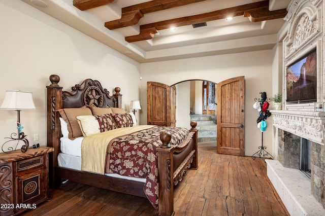 bedroom with beam ceiling, a high end fireplace, and dark hardwood / wood-style flooring