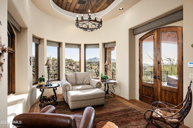 living room featuring french doors, wooden ceiling, a tray ceiling, dark wood-type flooring, and a notable chandelier