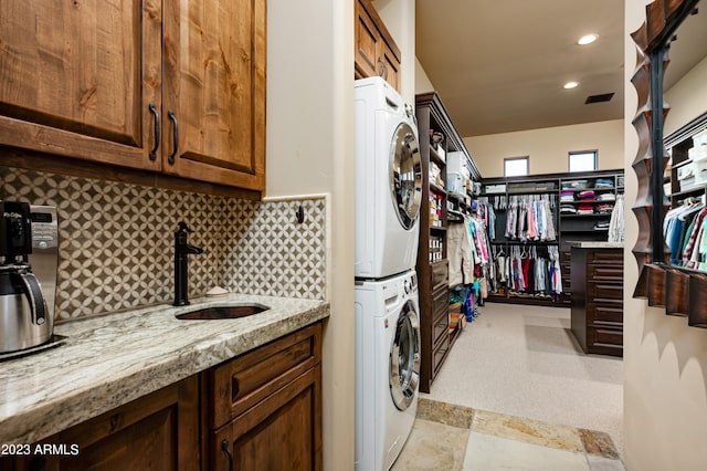 laundry room featuring stacked washer / drying machine, sink, and light tile floors