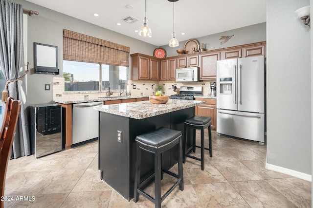 kitchen with a kitchen bar, stainless steel appliances, tasteful backsplash, light stone counters, and a center island