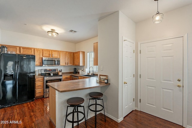 kitchen featuring stainless steel appliances, a peninsula, a sink, visible vents, and dark wood-style floors