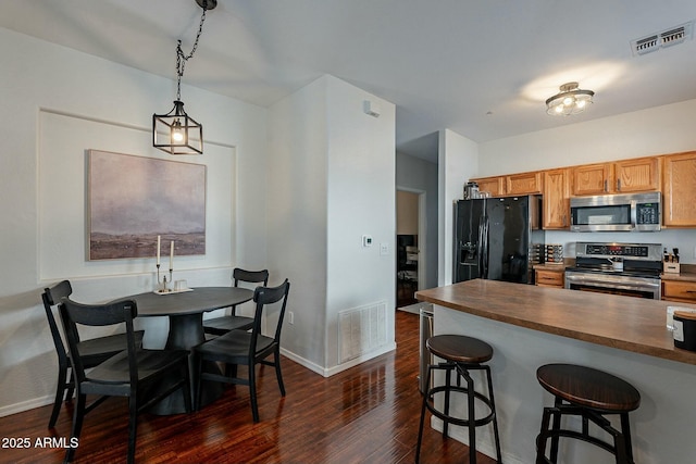 kitchen with appliances with stainless steel finishes, a breakfast bar, dark wood-style flooring, and visible vents