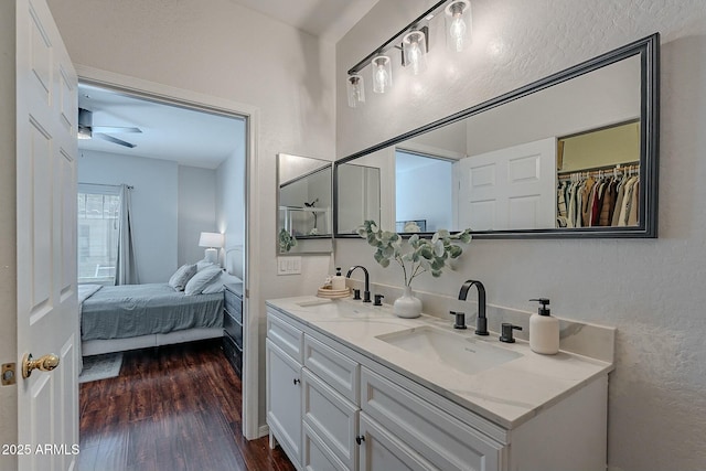 ensuite bathroom with double vanity, a textured wall, a sink, and wood finished floors