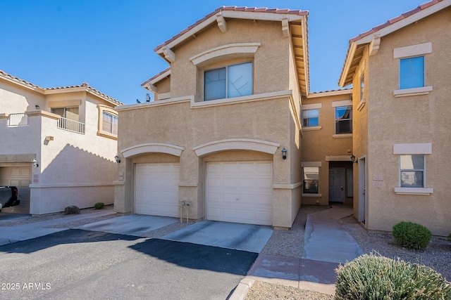 view of property with a garage, driveway, a tiled roof, and stucco siding