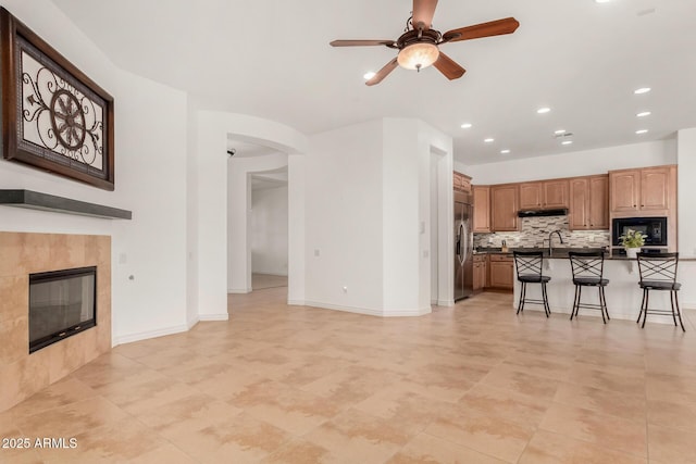 kitchen with a kitchen bar, stainless steel fridge with ice dispenser, an island with sink, a fireplace, and backsplash