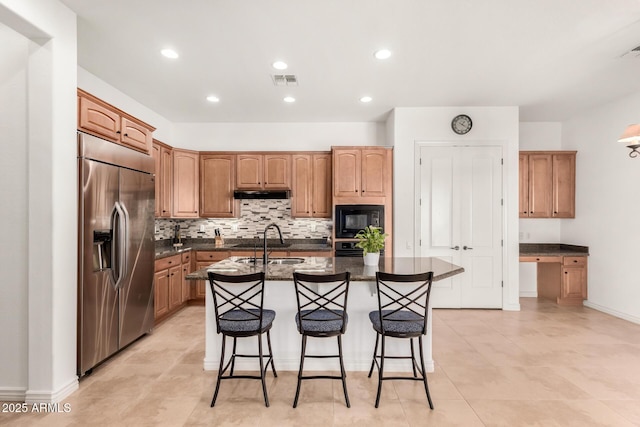 kitchen featuring dark stone countertops, built in appliances, an island with sink, a kitchen bar, and decorative backsplash