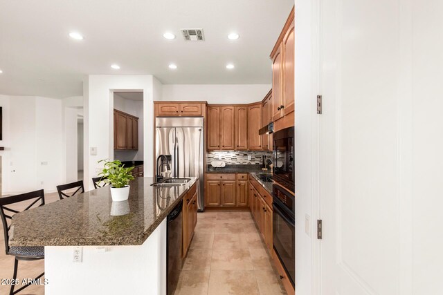 kitchen featuring a breakfast bar, dark stone countertops, backsplash, black appliances, and a center island with sink