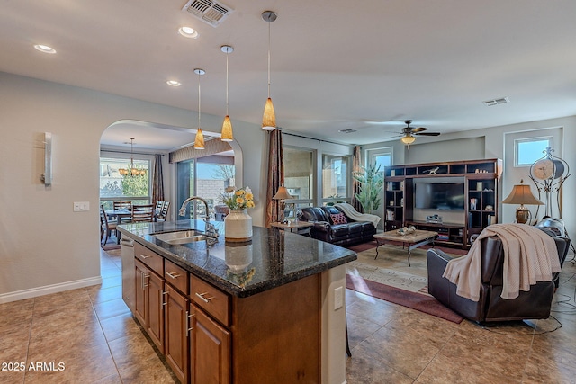 kitchen featuring sink, a breakfast bar area, hanging light fixtures, a center island with sink, and dark stone counters