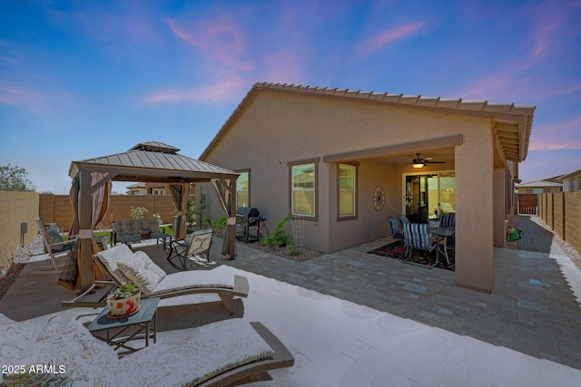 19560 W Valle Vista Way, Litchfield Park, AZ 85340 - patio terrace at dusk with a gazebo, a ceiling fan, a fenced backyard, a grill, and an outdoor hangout area