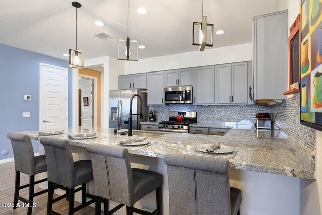 19560 W Valle Vista Way, Litchfield Park, AZ 85340 - kitchen with stainless steel appliances, visible vents, light stone countertops, gray cabinetry, and tasteful backsplash