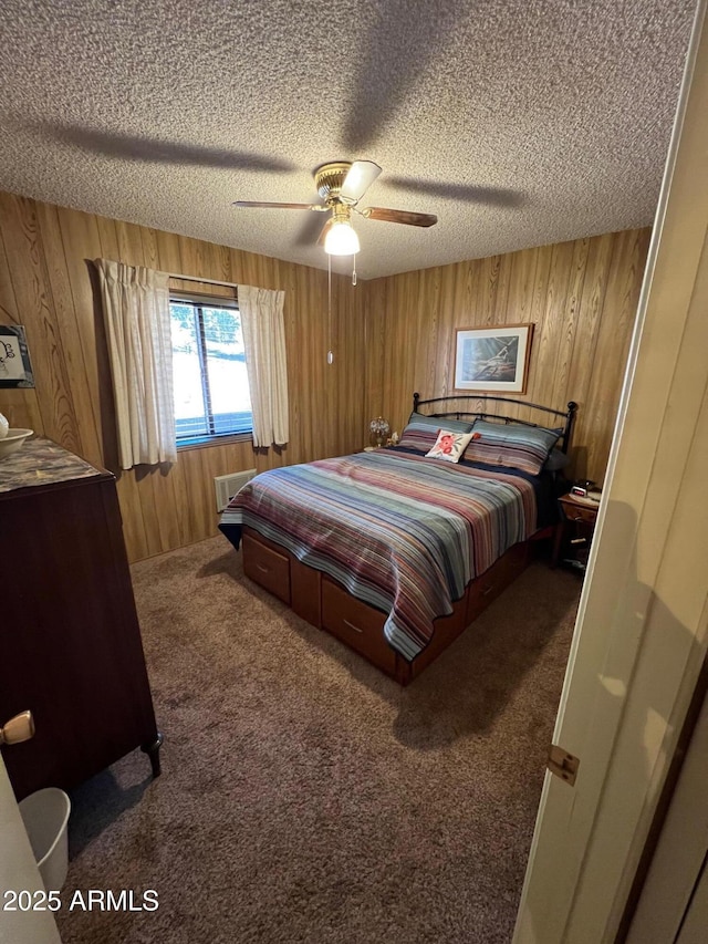 bedroom featuring a textured ceiling, dark carpet, wood walls, and ceiling fan