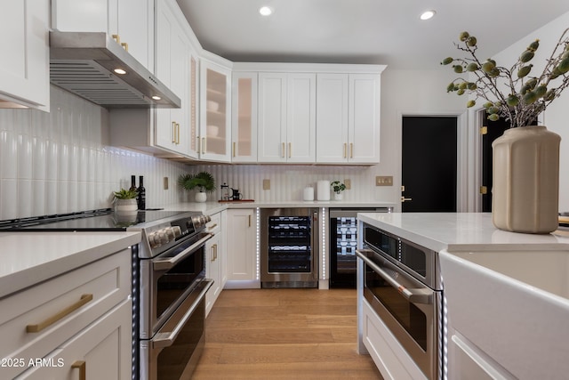 kitchen with white cabinets, appliances with stainless steel finishes, light countertops, extractor fan, and wine cooler