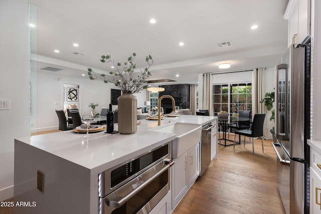 kitchen with visible vents, a center island with sink, a sink, open floor plan, and stainless steel appliances
