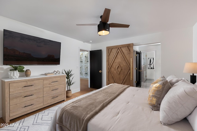 bedroom featuring a ceiling fan, baseboards, ensuite bathroom, and light wood finished floors