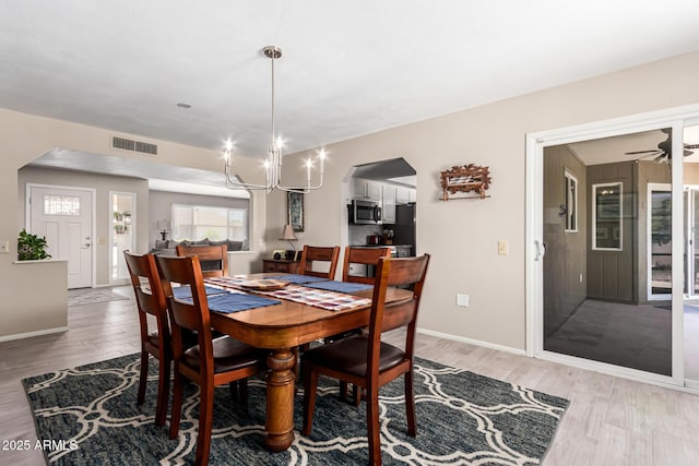 dining space with arched walkways, an inviting chandelier, light wood-type flooring, baseboards, and visible vents