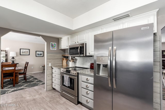 kitchen with light stone countertops, stainless steel appliances, tasteful backsplash, visible vents, and white cabinetry
