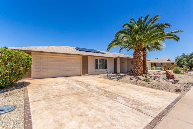 ranch-style home with driveway, brick siding, solar panels, and a garage