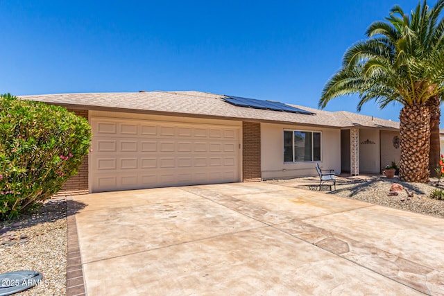 single story home with roof mounted solar panels, driveway, a garage, and brick siding