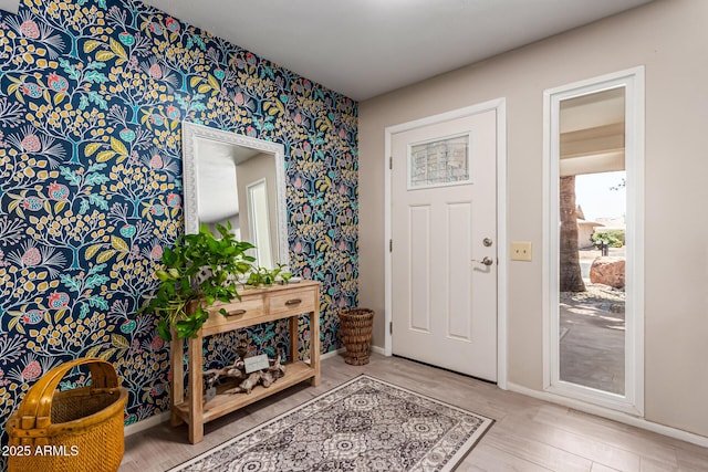 foyer with an accent wall, wallpapered walls, and baseboards